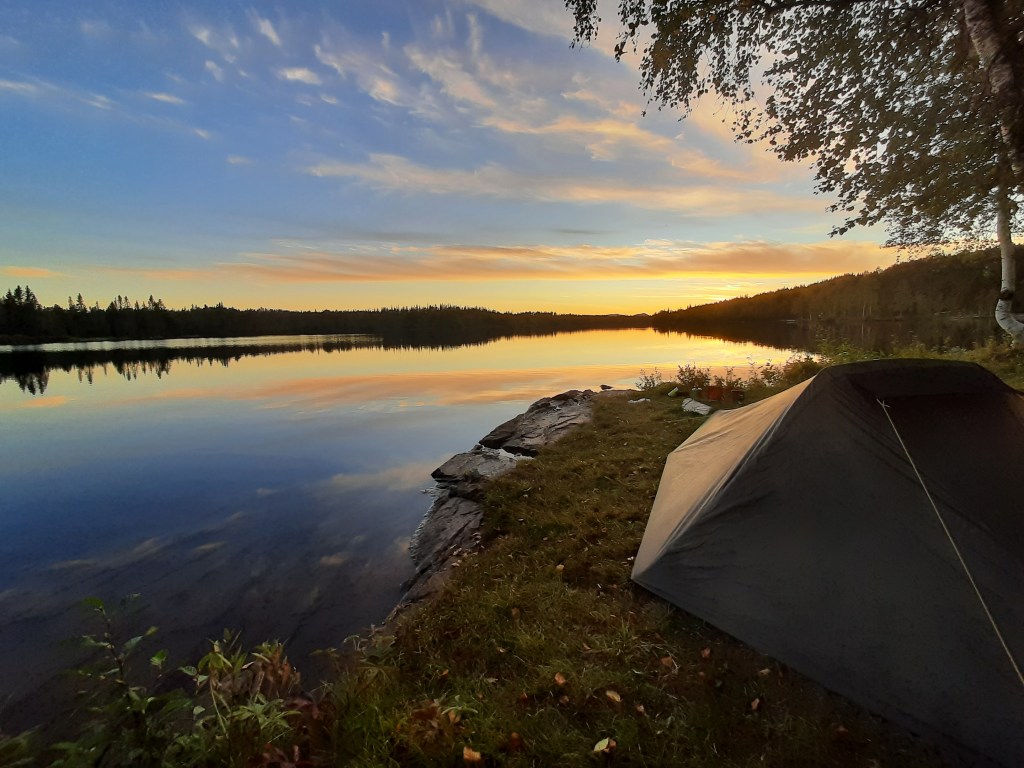 Blick auf einen malerischen Sonnenuntergang direkt neben einem See, der die schönen Zeltplätze in Norwegen widerspiegelt.